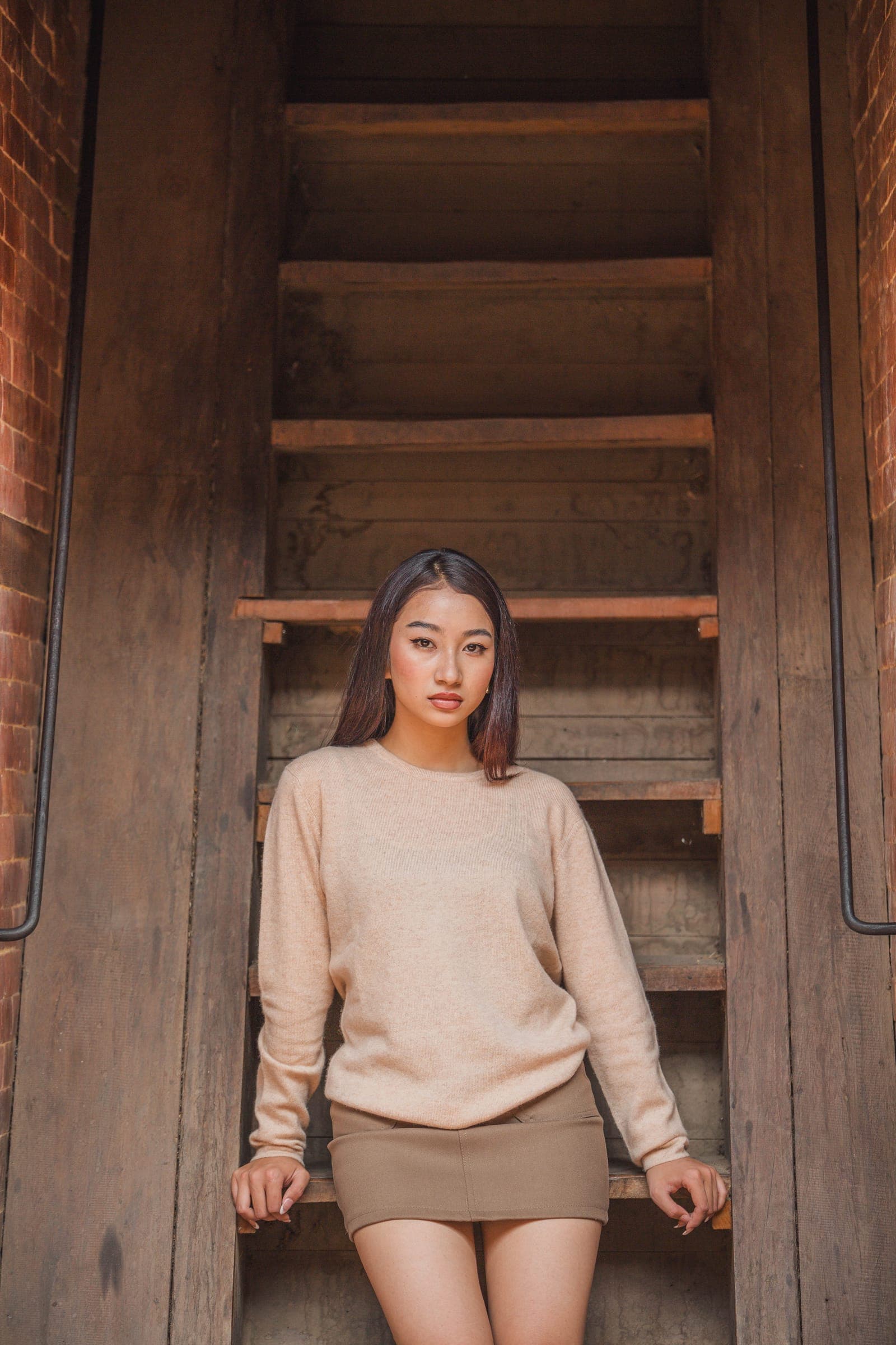 A woman in a beige cashmere sweater sits on a steep wooden staircase
